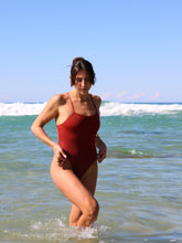 Woman in a JAYD Cinnamon coloured Isla tie-back one piece standing on a beach with ocean waves in the background